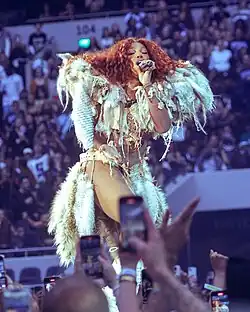 SZA performing intensely in front of a cheering crowd; some concertgoers are recording videos