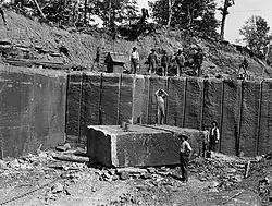 Workers standing in a quarry with a large stone block.