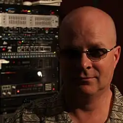 Kevin Williams wearing shaded glasses, juxtaposed with a stack of musical equipment