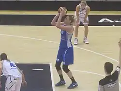 A basketball player lines up a penalty throw. She is wearing a blue top and baggy shorts.