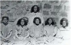 Black and white photograph showing seated people. The queen is in the second row.