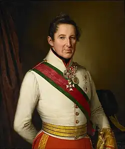 Painting shows a clean-shaven man wearing a white military uniform with a red sash and red breeches.