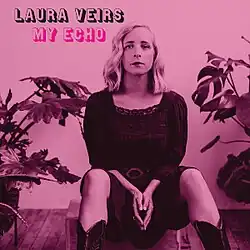 A pink and magenta monochromatic photo of Veirs seated