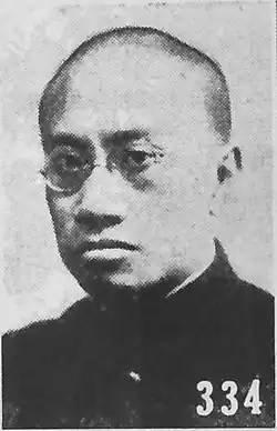 Black-and-white portrait of a man with shaved hair and glasses