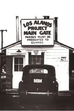 small guard shack with sign stating that passes must be presented to guards, a nineteen forties era car is parked there