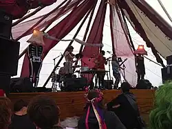 Lulu and the Lampshades, Bestival 2010; left to right (without the "Lampshades"): Dan Blackett (drums, hidden), Heloise Tunstall-Behrens (violine), Luisa Gerstein (ukulele), Jemma Freeman (electric guitar)