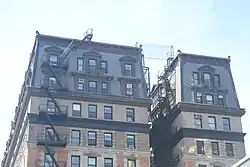 The upper stories of the 109th Street facade, including the mansard roof, as seen from the north. The facade is asymmetrical, with three windows to the right and five windows to the left of a light court. Below the mansard roof, the facade is clad with brick.