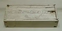 White rectangular box with small cracks and a long line of hieroglyphs along the entire length of the lid, at its centre