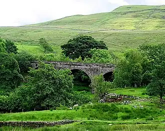 A stone viaduct in an upland environment, surrounded by trees and bushes