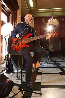 A man wearing dark clothihng is performing in front of a microphone while holding an electric guitar.