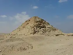 The prominent but crumbling remains of a pyramid, with its original, well-preserved stepped structure exposed underneath the rubble