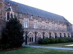 A Gothic-style exterior showcases Cathedral-like windows with the intricate framework and dark, colorful stone, with bushes and grass in the foreground