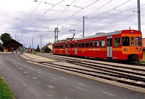 Red and orange train on a railway line next to platform shelter