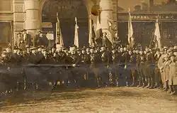 Uniformed men posing for a photo with several flags in the background