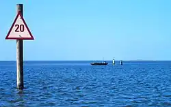 A small boat and wading fishermen in shallow water by a beach