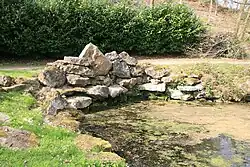A colour photograph of an arrangement of light-brown rocks at the head of an inlet from a lake