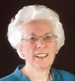 Photo of an elderly lady with white hair, eyeglasses, pearl necklace, and a blue shirt