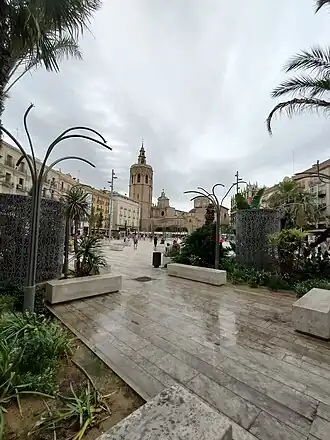 a view through stone benches and public art across a stone plaza with a church in the distance