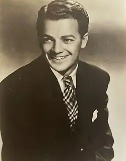 A man wearing a suit and tie is smiling while looking towards the right.