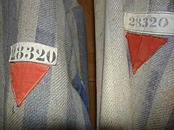 Red triangle emblems of a political enemy on a Dachau detainee's clothing. The white cloth-tape above bears the ID number 28320. ^