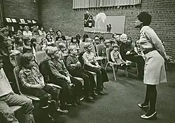 Rita Cox standing and telling story in front of room of seated children