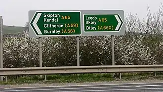 Pair of green trunk road signs, pointing left to Skipton and Kendal and right to Leeds and Otley on the A65, with other destinations indicated on other roads