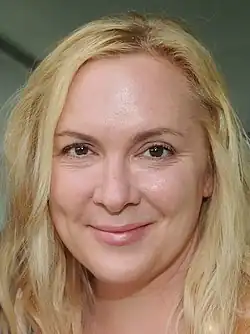 A woman with shoulder-length blonde hair smiles into the camera