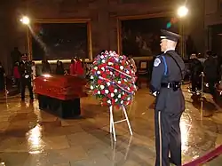 Rosa Parks's casket being guarded by two uniformed men in the capitol rotunda. A huge bouquet of red and white flowers is visible in the foreground.