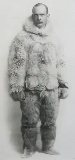 A black-and-white photo of a man wearing animal-skin clothing for cold-weather travel