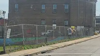 The fence of a park with a thin blue line U.S. flag and flowers in the middle of the fence.