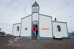 A low slung white and blue clapboard building with a single central steeple.