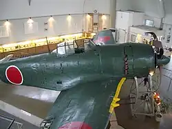 Color photo of a dark green single engined monoplane aircraft inside a room