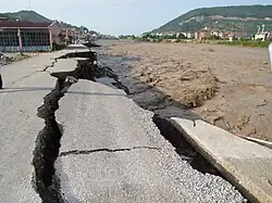 road with large cracks being washed away by a roiling brown river