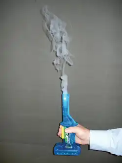 A hand grasping a small blue apparatus with white smoke emerging from its top