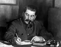 Photograph of Stalin writing at a desk with a pipe in his mouth