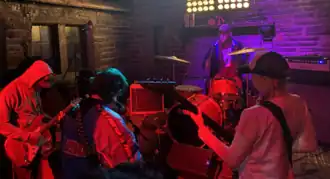 Three guitarists and one drummer. The guitarists are all in front of the stage facing away from the audience