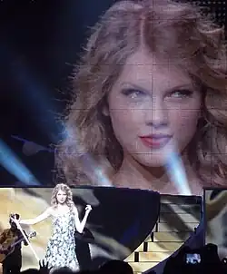Swift striking a pose onstage as the screen behind her shows a closeup of her face