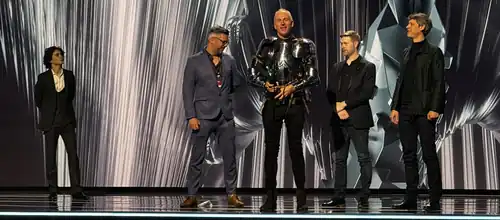 On stage, Timothée Chalamet stands to the left while four game developers accept an award at right, one dressed in armor.