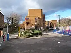A footpath stretches in a straight line into the distance, next to a large yellow rectangular building.
