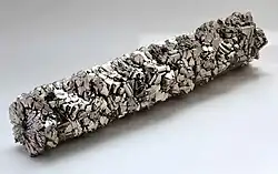 A bar of metal formed out of shiny metallic titanium crystals that appear to have grown from the center outwards