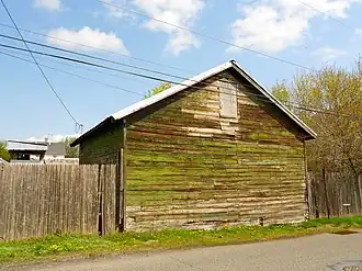 A weathered wooden shed covered with moss sits beside a gravel road.