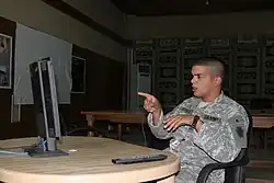 Waring a green US army suit in front of a LCD monitor