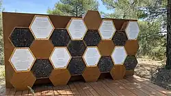 Hexagonal wooden boxes, beehives. Text with information is plastered on them.