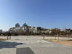 A fountain, and behind it a large rocky hill inside the park (2023)