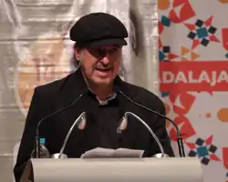 Un hombre vestido de colores oscuros habla al micrófono en un estrado.