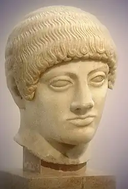 Efebo Rubio o Kuros rubio, ca. 490-480 a.C., Museo de la Acrópolis de Atenas. Fue encontrada junto con parte de la pelvis, al noreste de la Acrópolis de Atenas en 1923. La representación estereotipada de los rizos del pelo son un rasgo arcaico. Ha sido atribuido a la generación de maestros de Fidias (Hegias de Atenas o Ageladas de Argos). El nombre de rubio se debe a los restos de policromía que se han conservado.[13]​