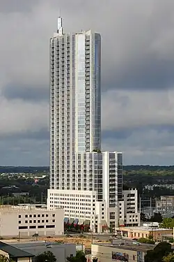 View of the 360 Condominiums from the north; the building has a blue glass facade; there is a setback 1/3 of the way up and a spire on the top of the tower.
