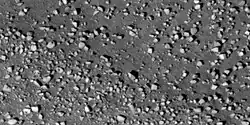 Vista cercana de los cantos rodados a lo largo del borde del cráter Los cantos rodados son aproximadamente del tamaño de automóviles o casas pequeñas. Fotografía tomada con HiRISE bajo el programa HiWish.