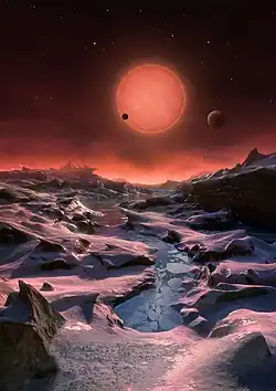 Esta ilustración muestra una vista imaginaria de la superficie de uno de los tres planetas que orbitan a una estrella enana ultrafría a tan solo 39 años luz de la Tierra, descubierto usando el telescopio TRAPPIST, instalado en el Observatorio La Silla de ESO. Estos mundos tienen tamaños y temperaturas similares a los de Venus y la Tierra y son los mejores objetivos encontrados hasta ahora para la búsqueda de vida fuera del sistema solar. Son los primeros planetas descubiertos alrededor de una estrella tan pequeña y débil. En esta ilustración, uno de los planetas interiores es visto en tránsito a través del disco de su pequeña y tenue estrella.