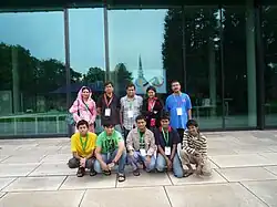 Diez personas mirando hacia adelante, en dos filas de cinco. En la fila delantera hay cinco adolescentes. Detrás de ellos hay cuatro adultos y una persona que parece también ser un adolescente.